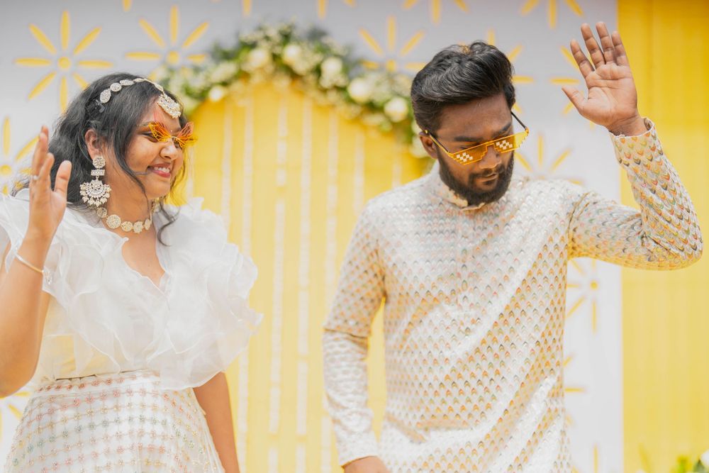 Happy couple in matching white outfits dancing against a decorated yellow wall.