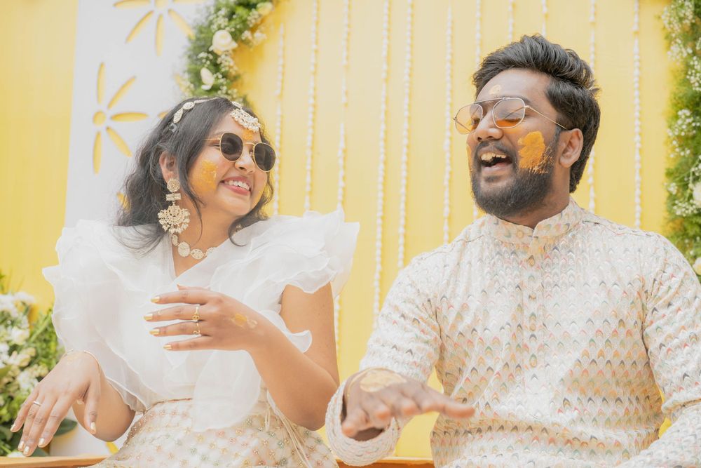 Couple sharing a joyful moment in white traditional attire against a yellow decorated backdrop.