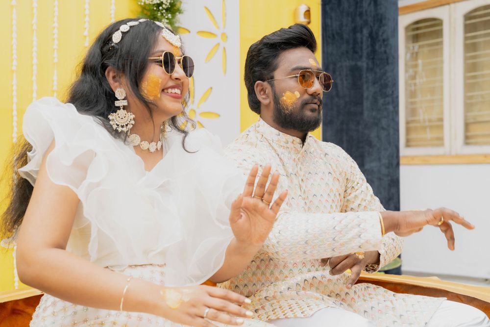 Couple in coordinated white attire dancing and enjoying a celebration against a yellow wall.