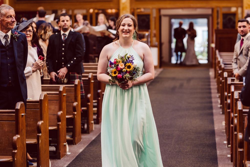 Bridesmaids in pastel dresses process through church carrying colorful floral bouquets.