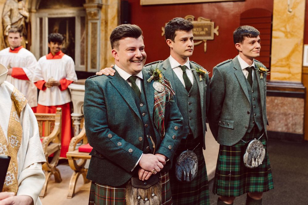 Groomsmen in dark suits and kilts gather in the church before the ceremony.