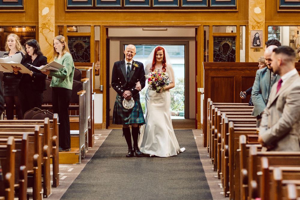 Wedding ceremony in a traditional church with ornate wooden pews and religious artwork on display.