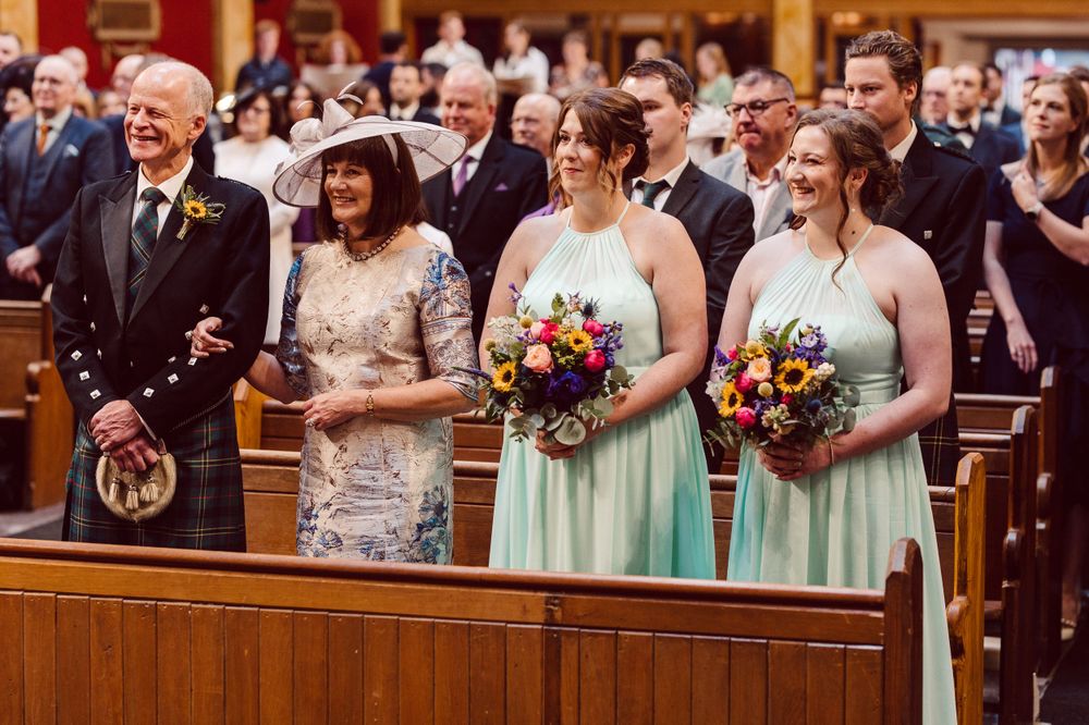 Wedding guests and bridesmaids in mint green dresses watching ceremony from church pews.