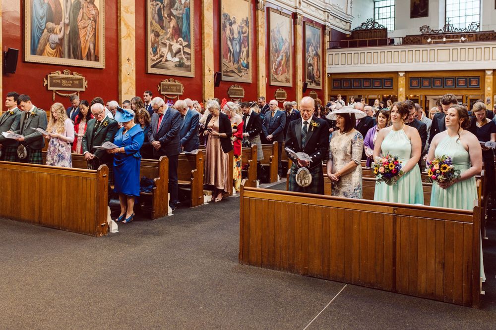 Wide view of wedding ceremony showing guests seated in wooden pews of traditional church.