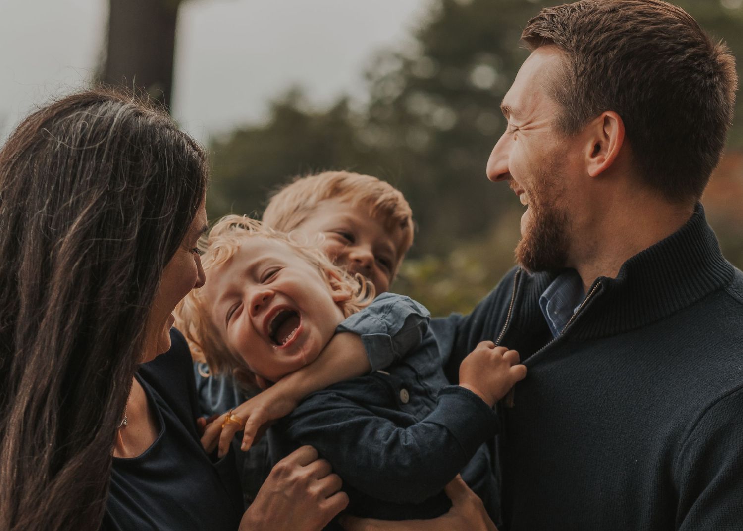 A candid outdoor photo showing a young family in Connecticut, USA, laughing and embracing together during a lifestyle photoshoot.
