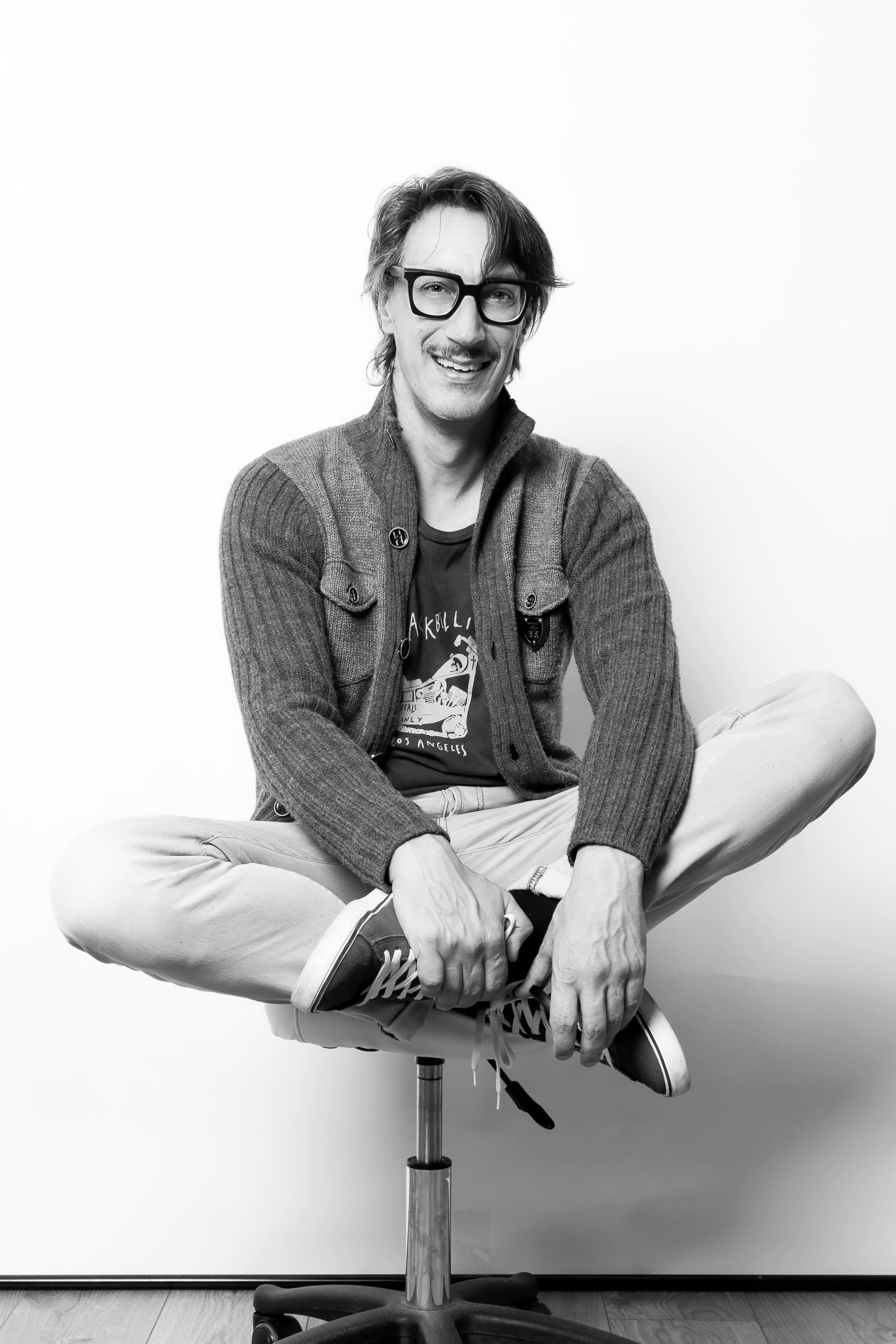 Black and white portrait of a person sitting cross-legged on a stool.