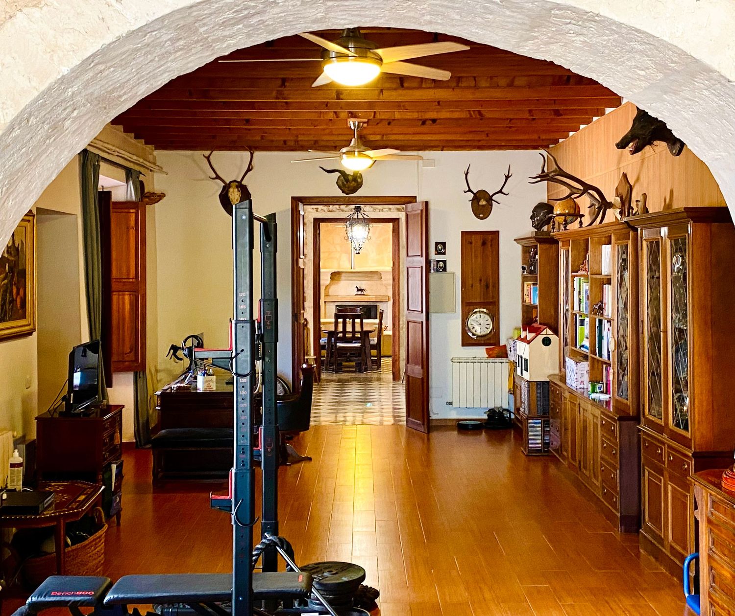 Long rustic hallway with wooden ceiling beams, hardwood floors, and mounted hunting trophies.