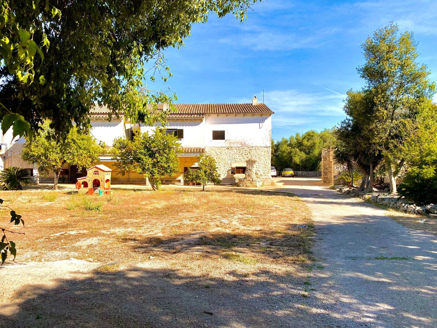 White country house with courtyard and trees in Mediterranean landscape.