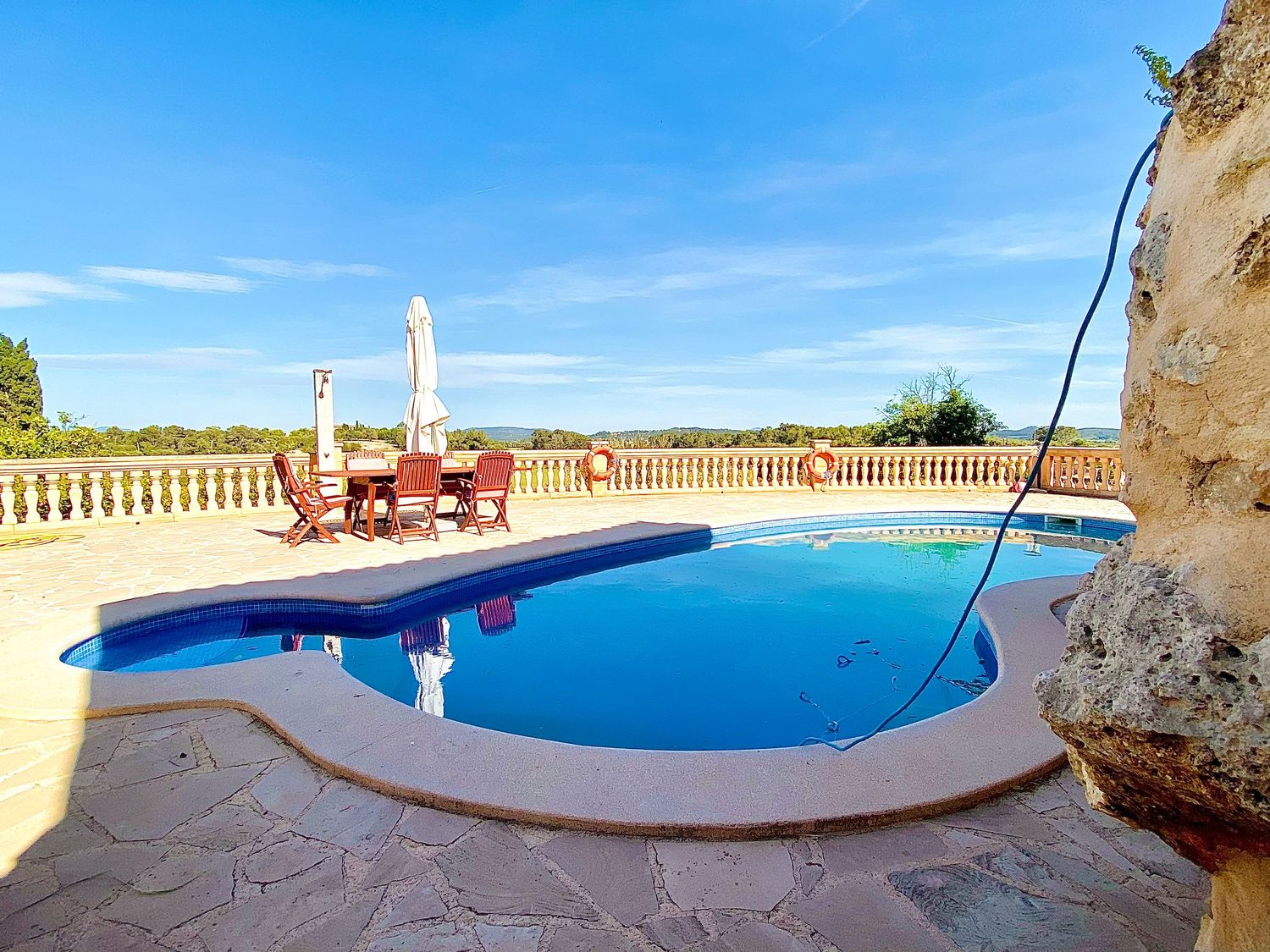 Oval swimming pool with lounge chairs and balustrade overlooking rural landscape.