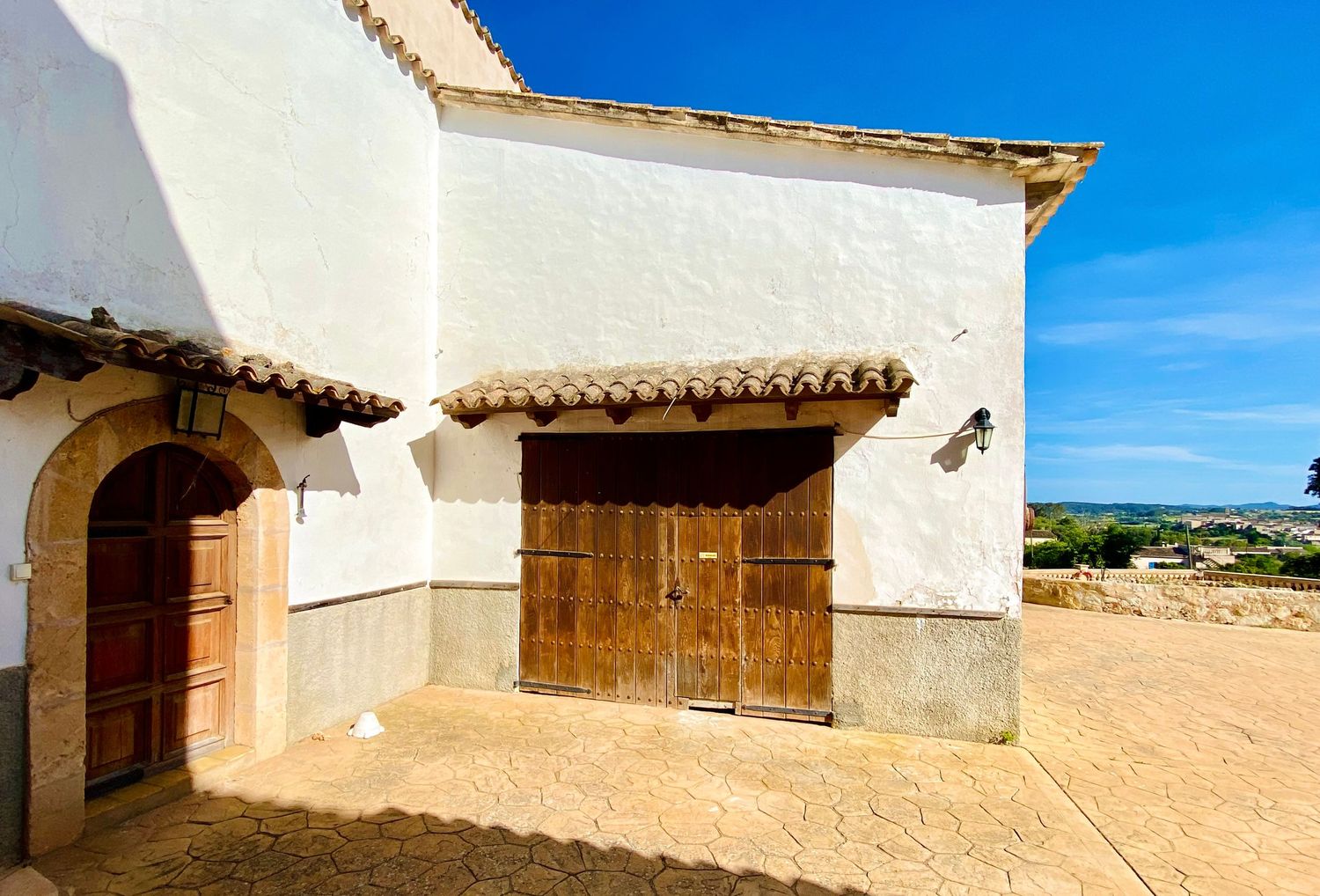 Traditional white stucco building with wooden doors and terra cotta tile roof detail.