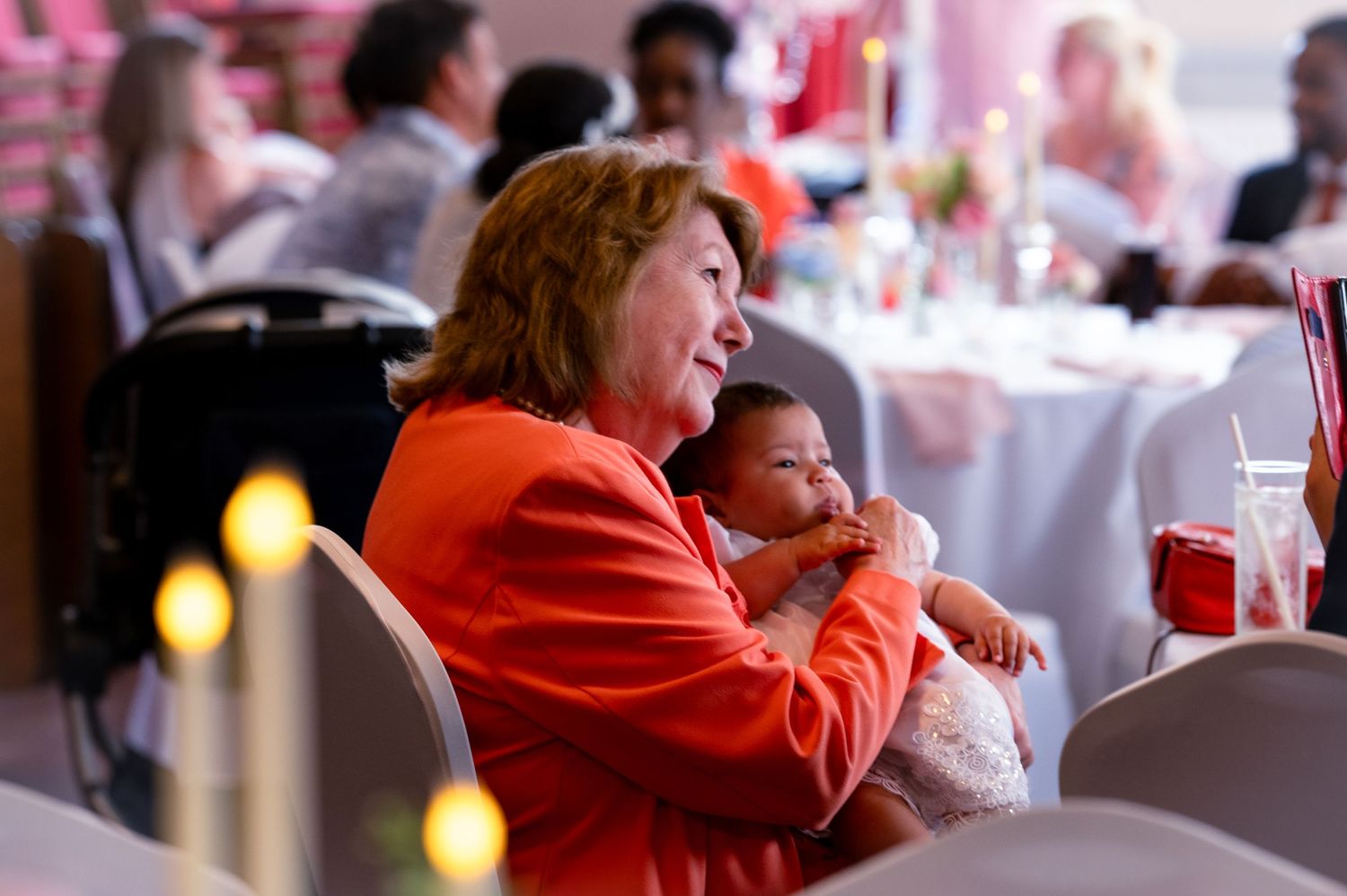 An intergenerational moment captured during a celebratory dinner event with candlelit tables and red accents.