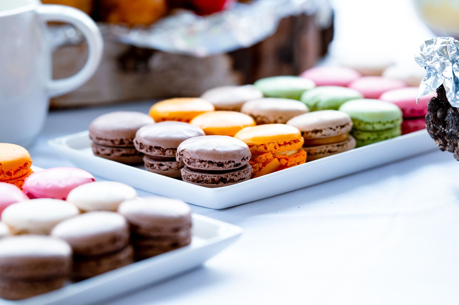 Colorful French macarons in various flavors arranged on white serving plates with blurred background.