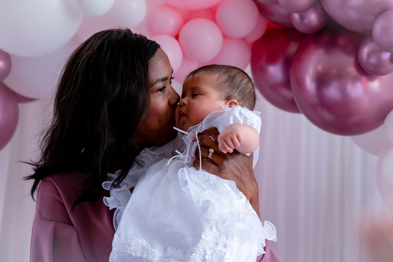 A tender moment between parent and baby against a backdrop of pink and purple balloons.