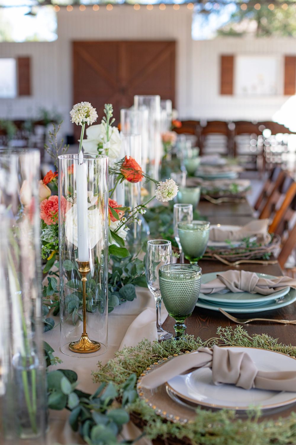 Elegant table setting with green glassware, white plates, and floral centerpieces featuring delicate greenery and flowers.