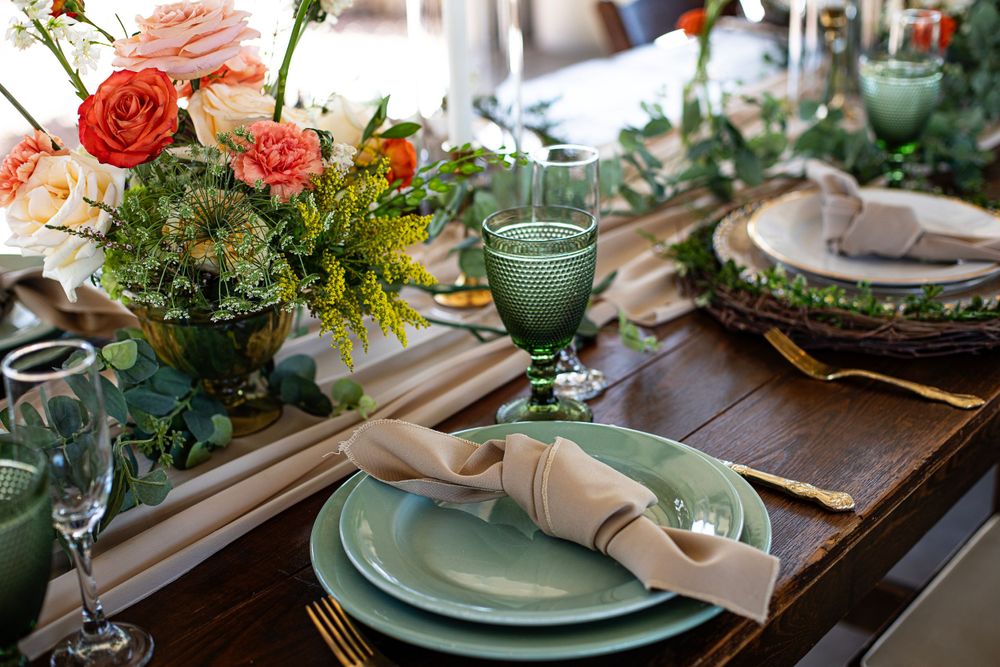 Wedding reception table decorated with coral roses, eucalyptus, and vintage-inspired green glassware.
