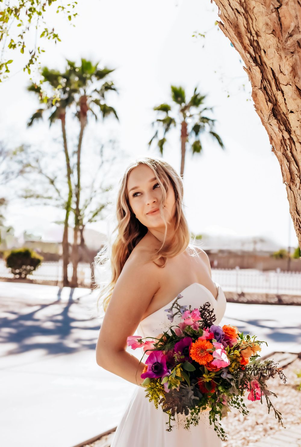 Bride holding vibrant wildflower bouquet with orange and pink blooms against desert scenery.
