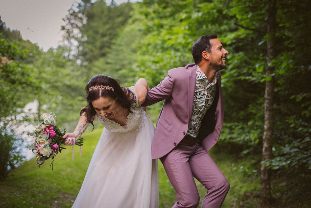 Playful couple in a garden wedding scene with groom in lilac suit and bride holding purple bouquet running together.