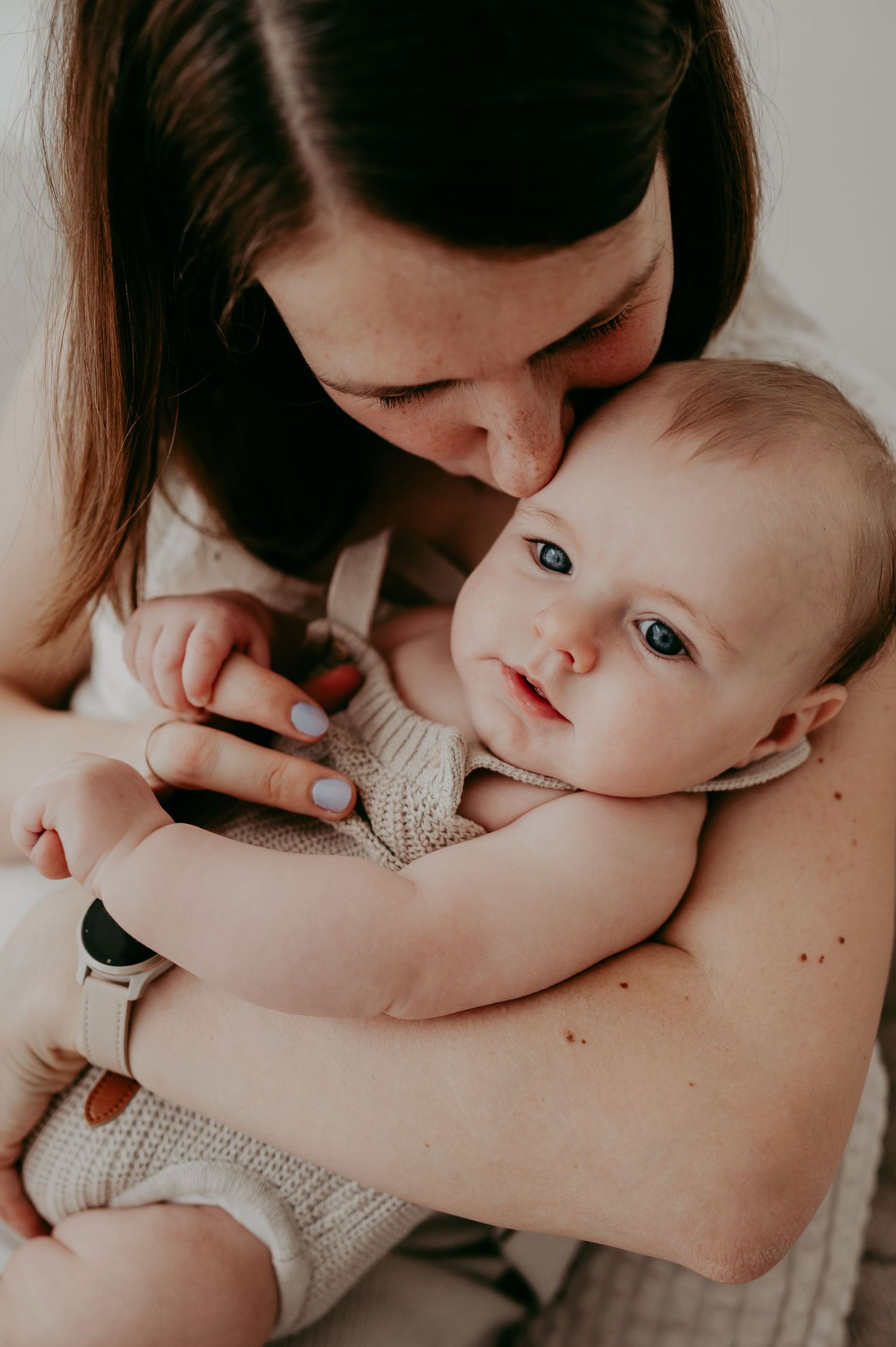 Tender moment between parent and infant in intimate indoor portrait.