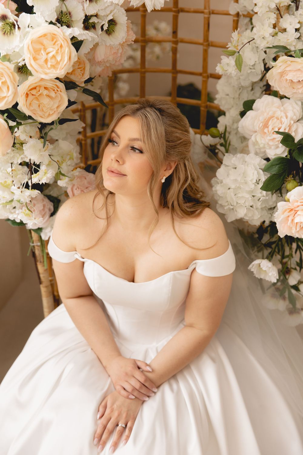Elegant bridal portraits against a floral backdrop with peach roses and white hydrangeas in an indoor setting.
