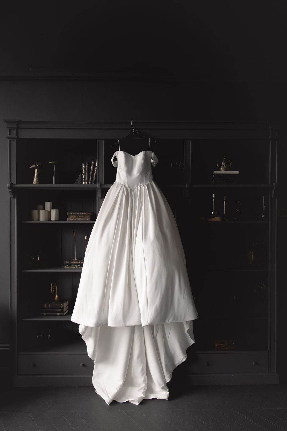 A white wedding dress photographed in a dark room with black built-in shelving creates a dramatic contrast.