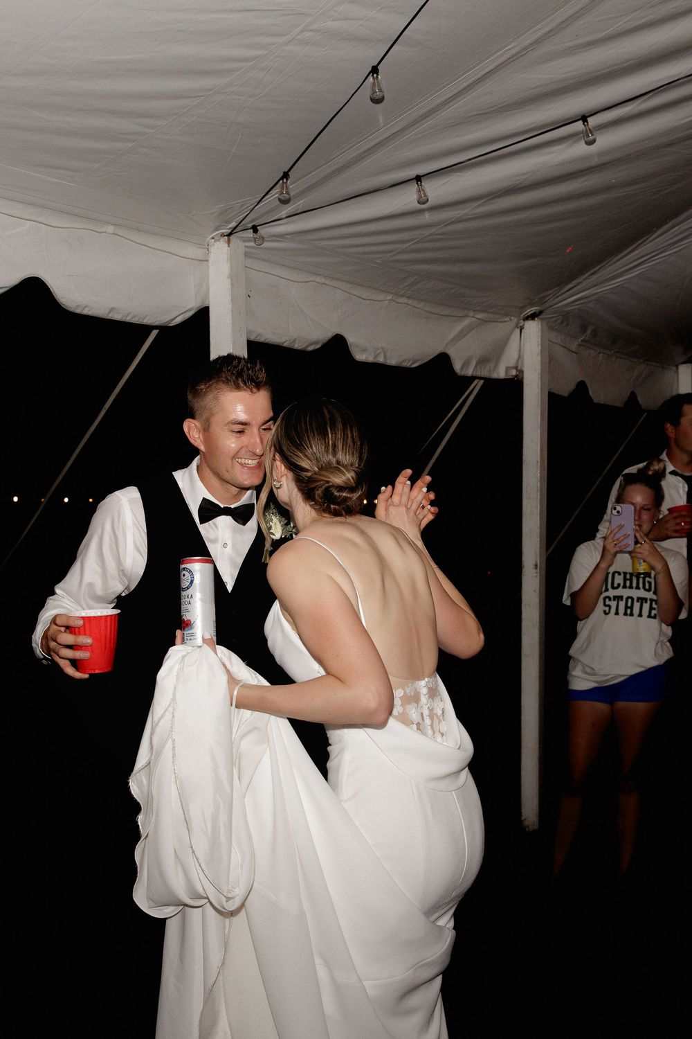 A couple shares a romantic dance moment under a white tent at a wedding reception.