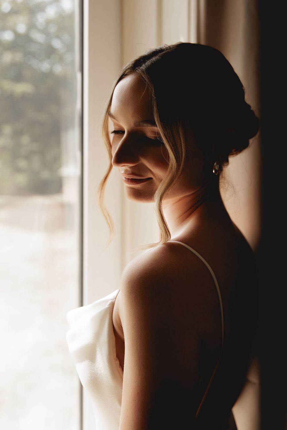 Silhouetted figure wearing headphones stands near window in warm backlit glow creating a dreamy atmosphere.