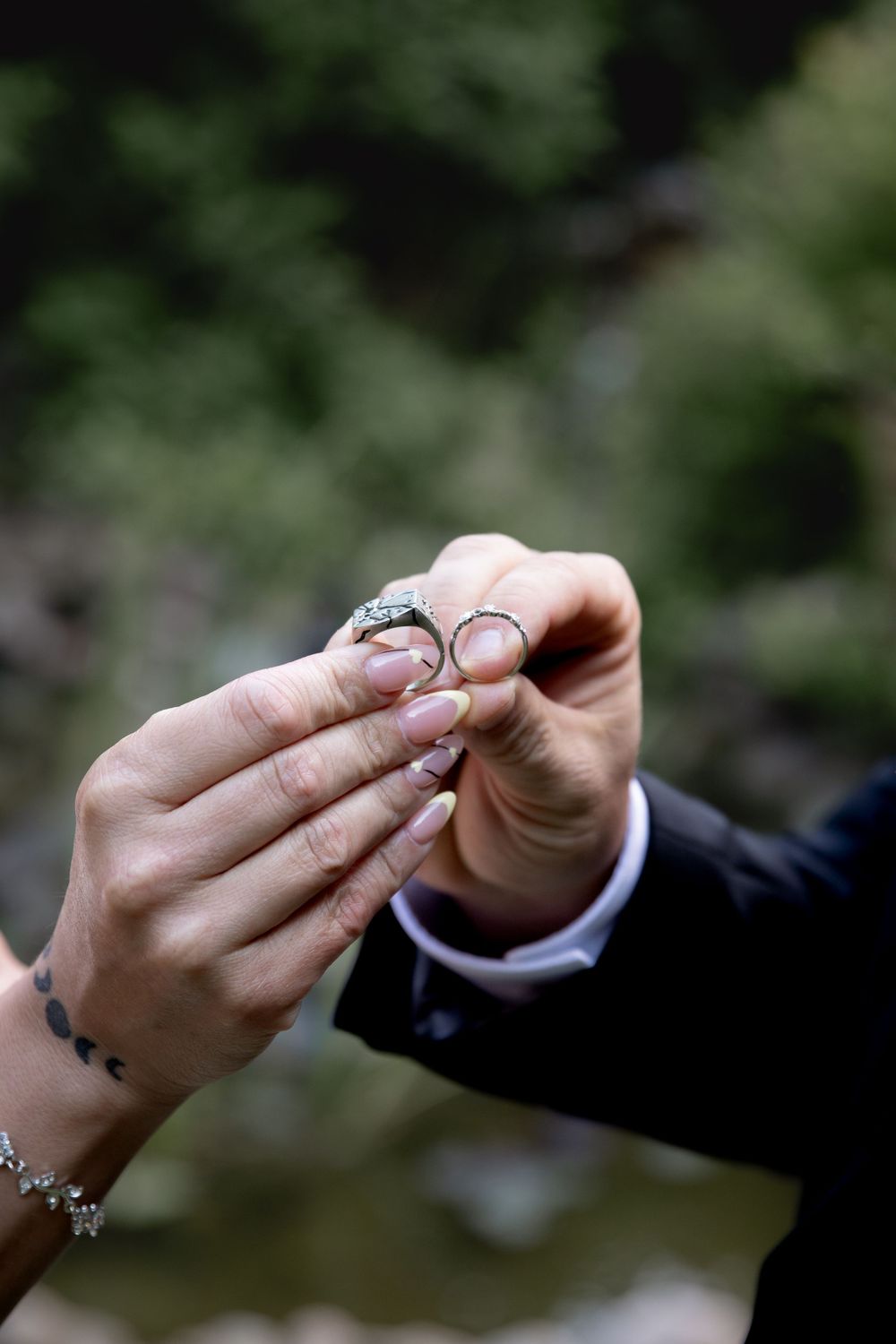 Close-up of hands holding wedding rings against a blurred natural background.