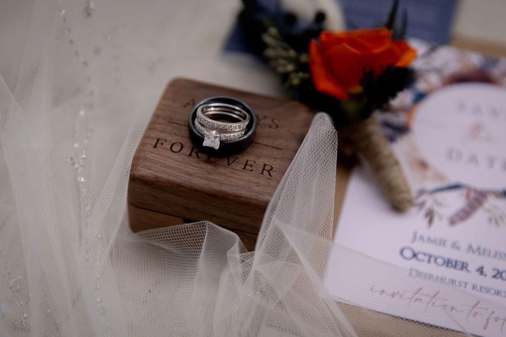 Wedding rings rest on a wooden box with 'FOREVER' engraving beside delicate invitation details.