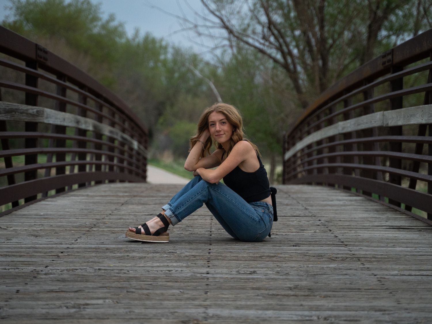 A contemplative person sits alone on a wooden bridge walkway.