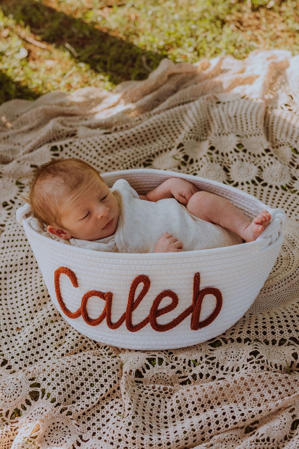 A sleeping newborn rests peacefully in a curved white basket on delicate lace fabric.
