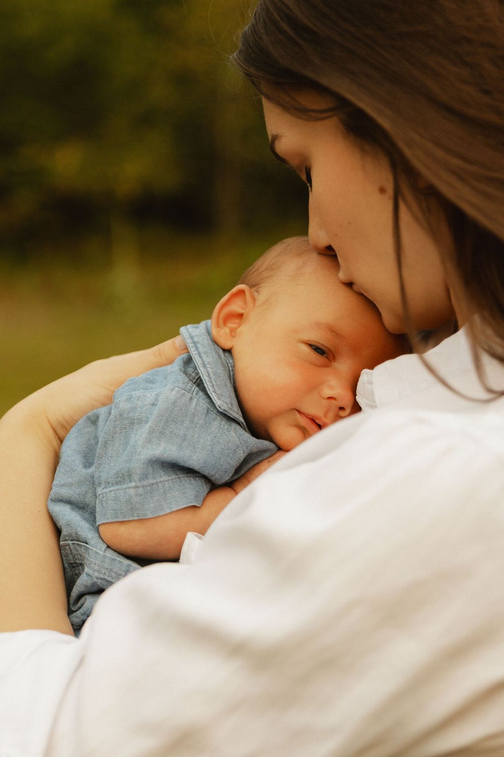 A close-up series showing a baby in a denim shirt slowly falling asleep while resting against someone in white clothing.