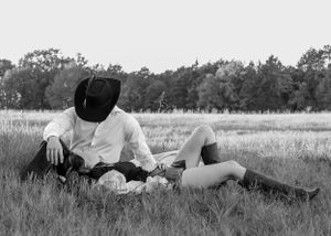 Black and white photo of a couple relaxing together in an open grassy field.