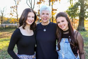 Three women including an older woman with white hair smile together in an autumn park.
