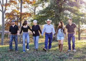 Six family members walking hand-in-hand through a grassy field surrounded by autumn trees.