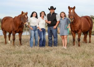 Family of four poses with two chestnut horses in an open field near a pond.