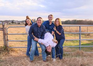Fun family of five posing at a farm gate with one member held upside down.