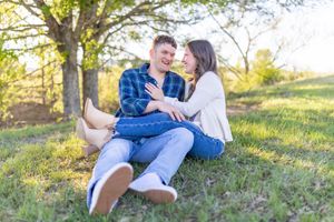 Happy couple sitting together on grass under a tree in golden sunlight.
