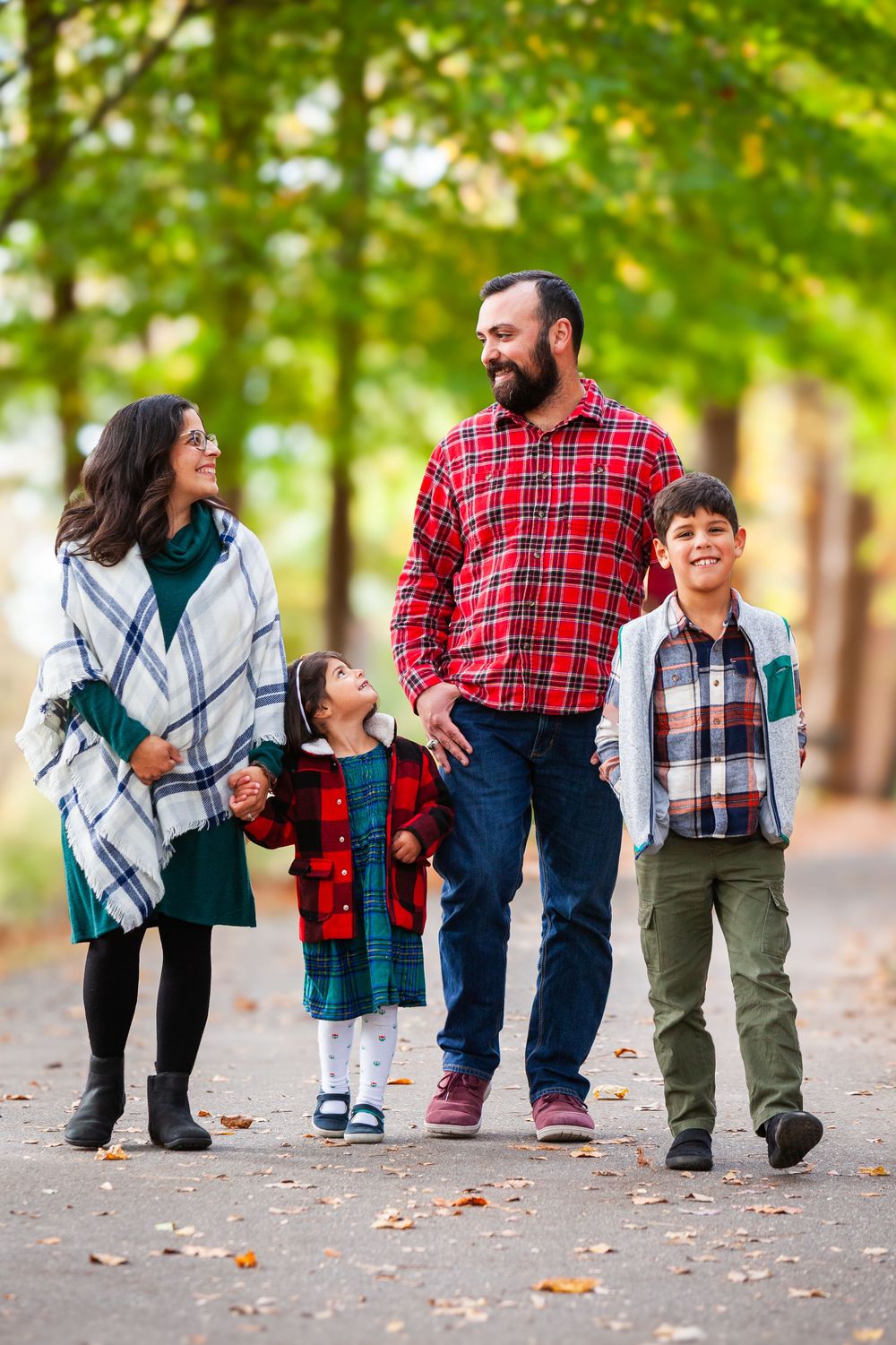 Happy family of four walking together on a tree-lined autumn path, holding hands and smiling warmly.