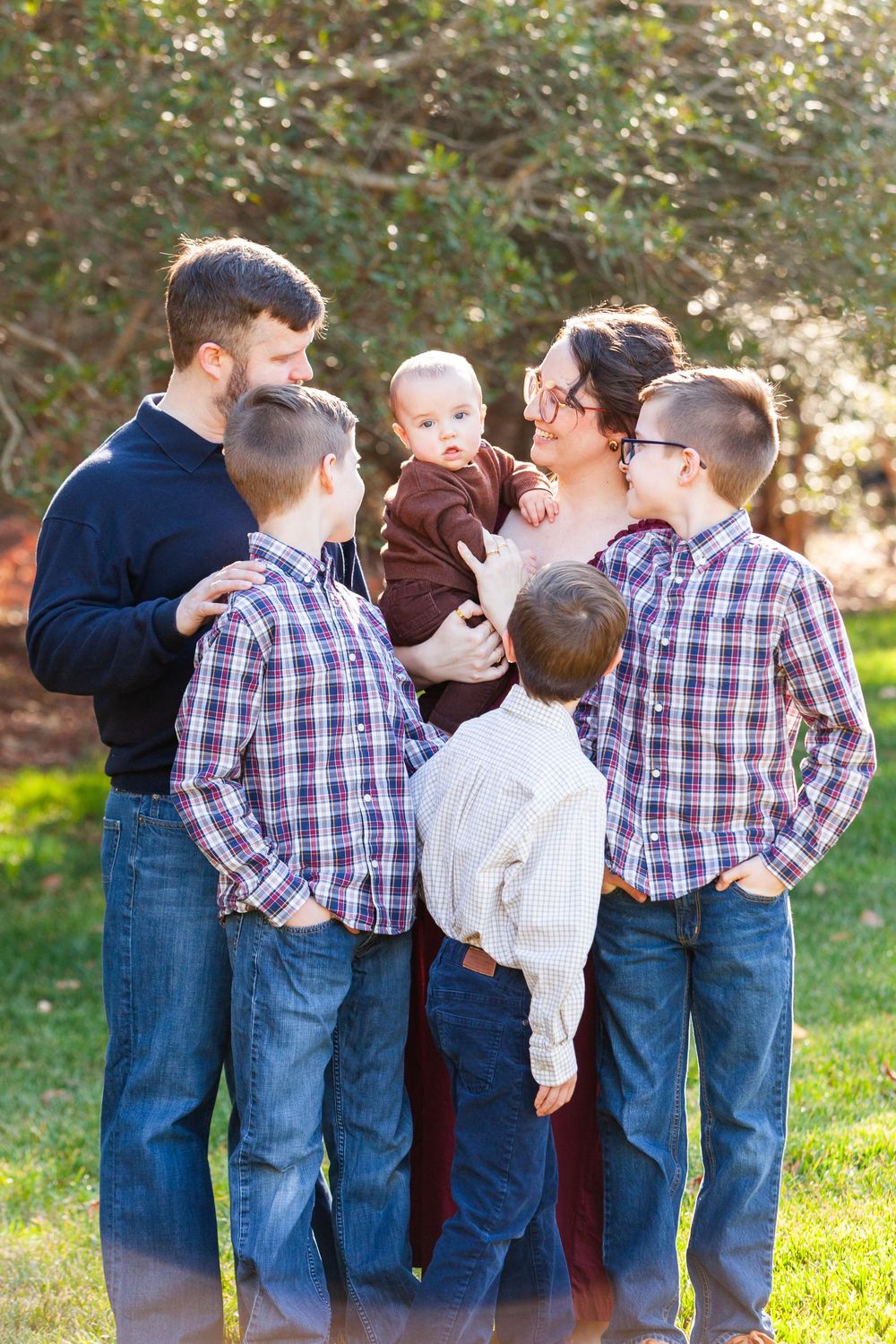 Family of six with four boys in plaid shirts posing together outdoors in a lush green park setting.