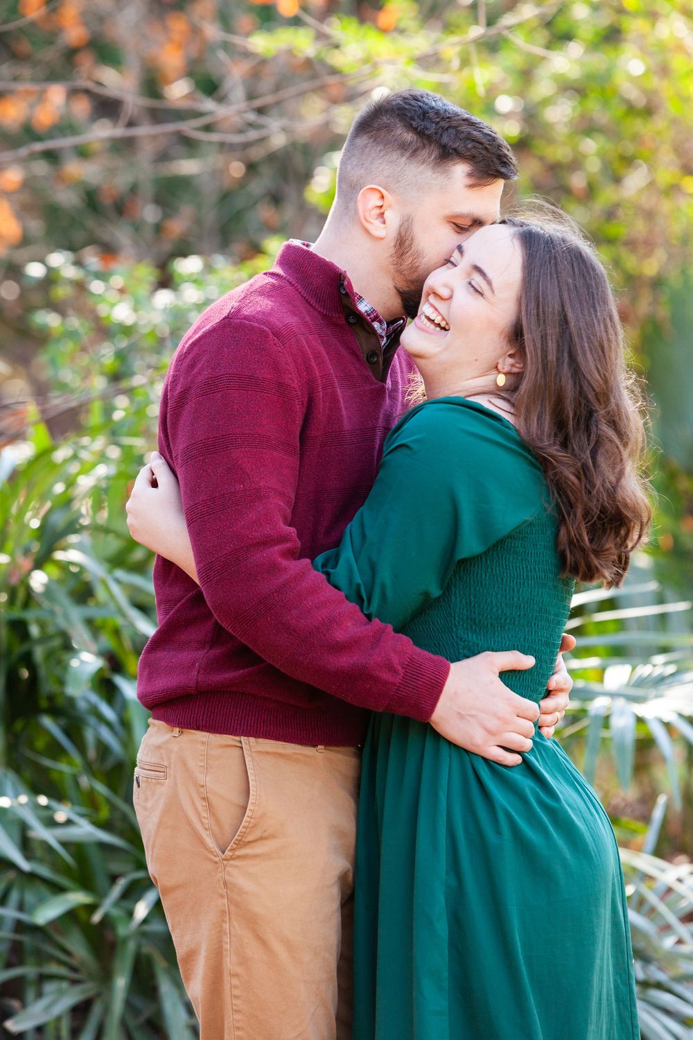 Happy couple laughing and embracing outdoors surrounded by colorful autumn foliage in warm sunlight.