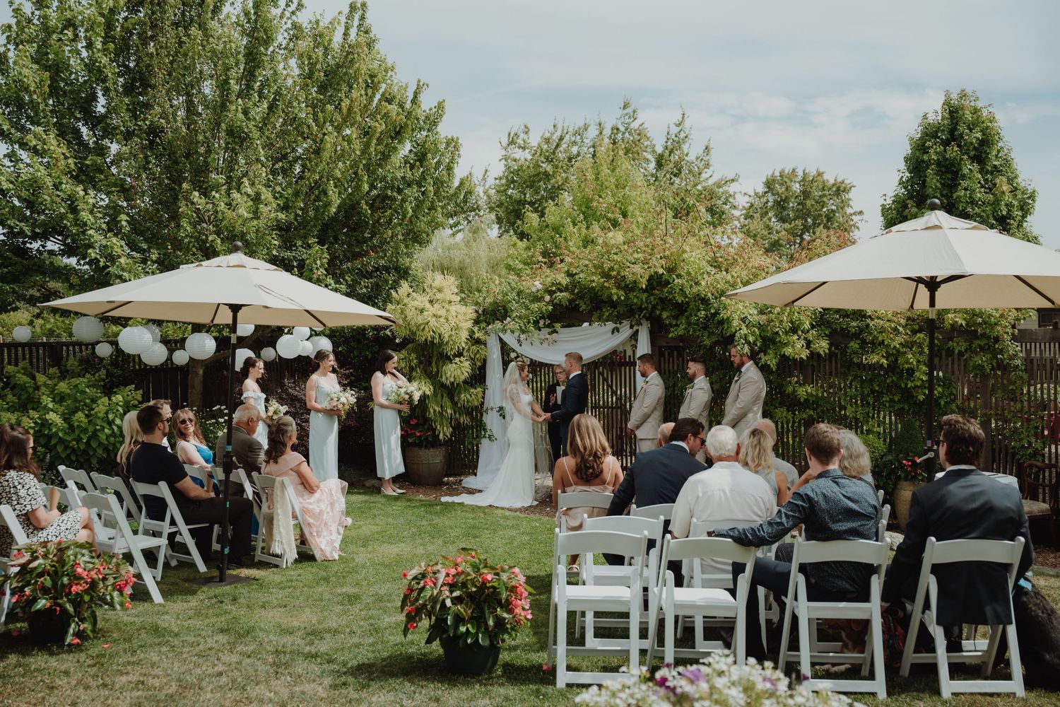 Outdoor garden wedding ceremony with guests seated on white chairs under large patio umbrellas. Vancouver Island Wedding, Victoria BC.