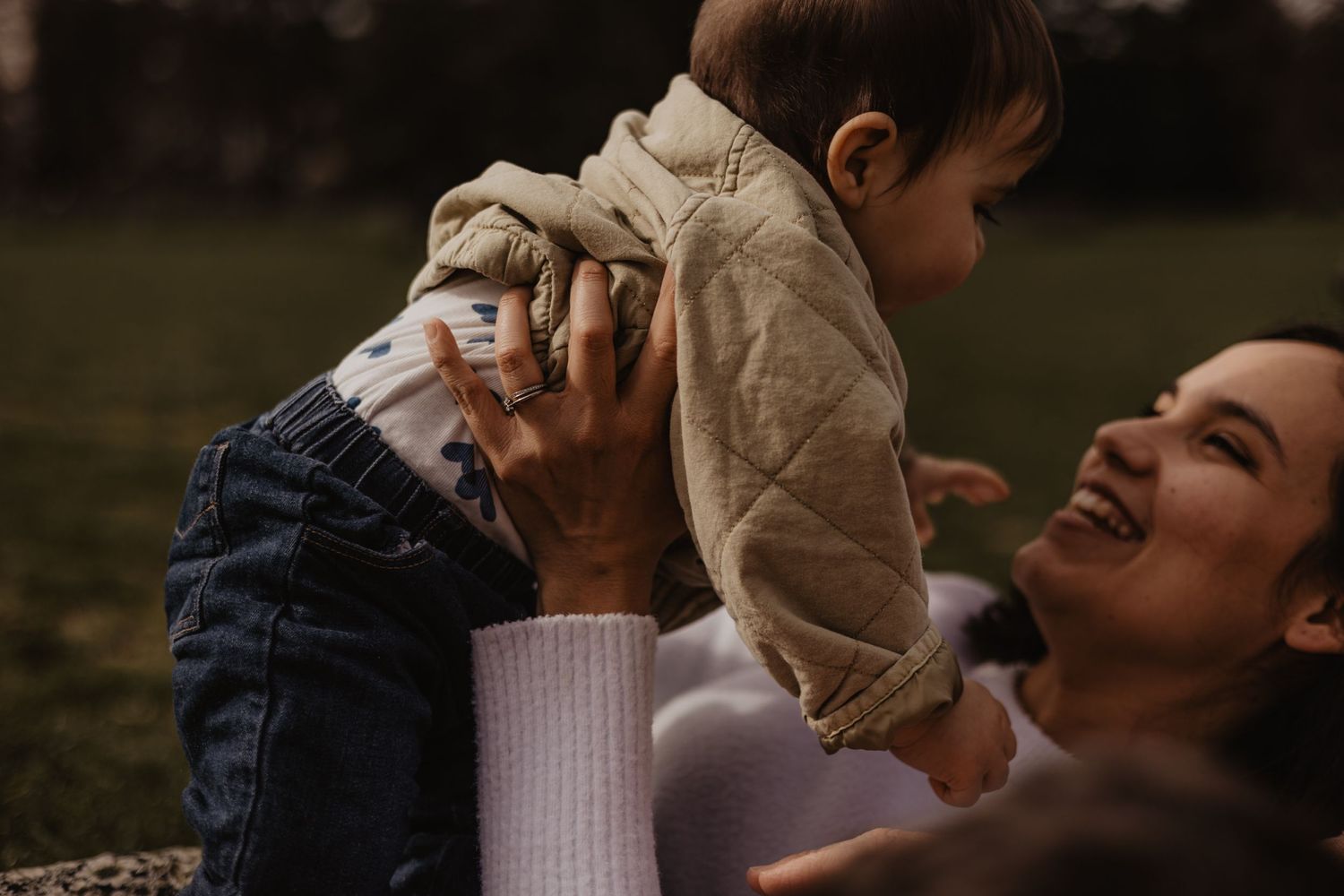 Portrait en extérieur d'une mère souriante jouant avec son bébé dans un parc. Moment de complicité.