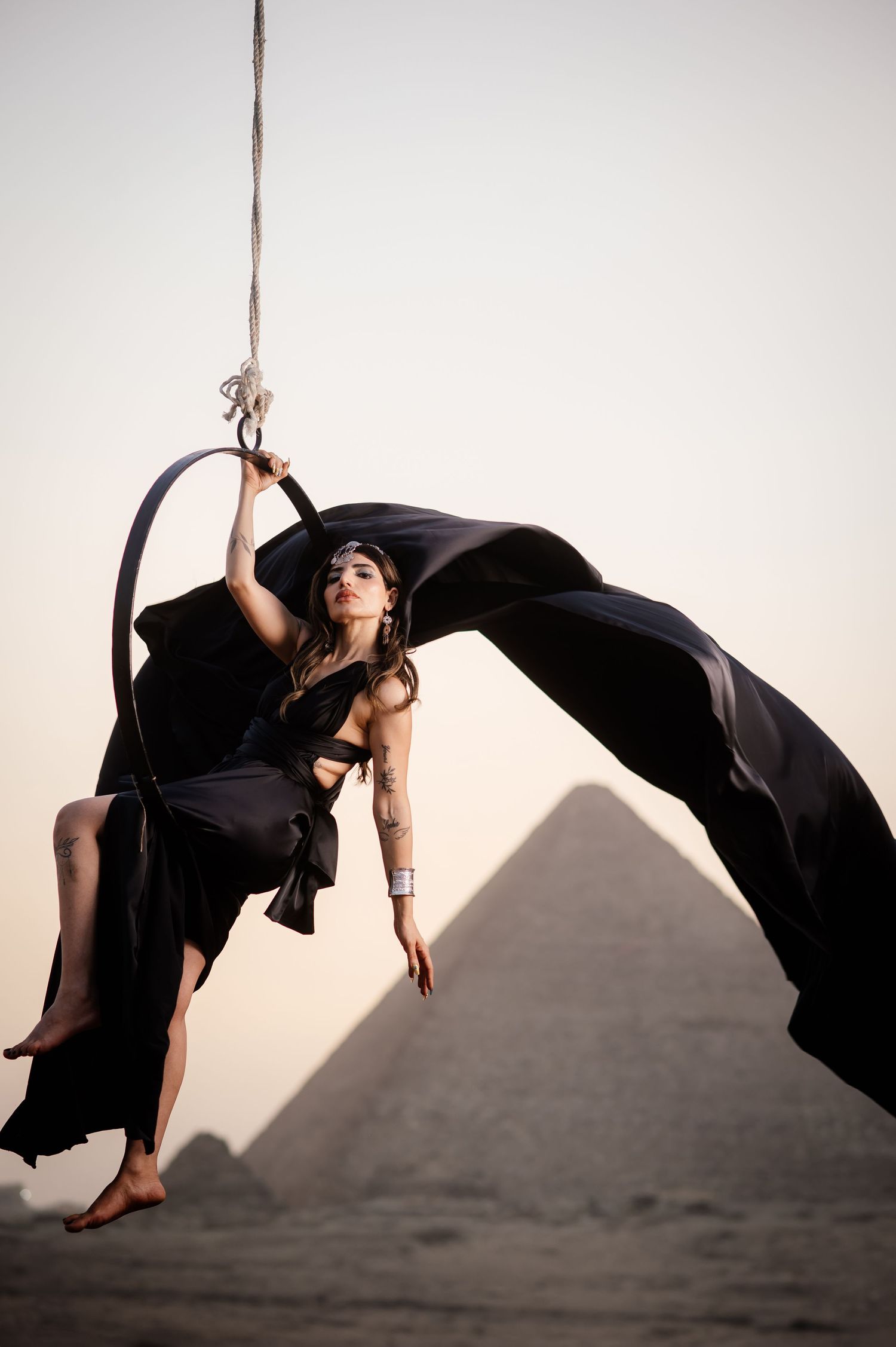 Aerial performer in black flowing fabric poses against pyramid silhouette.