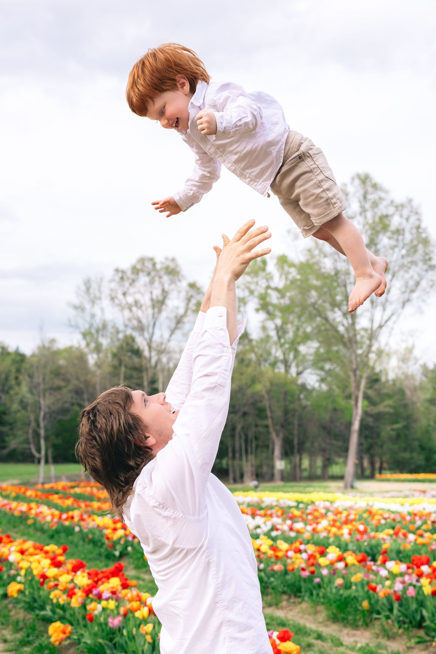 Parent lifts child joyfully above colorful tulip field on bright spring day.