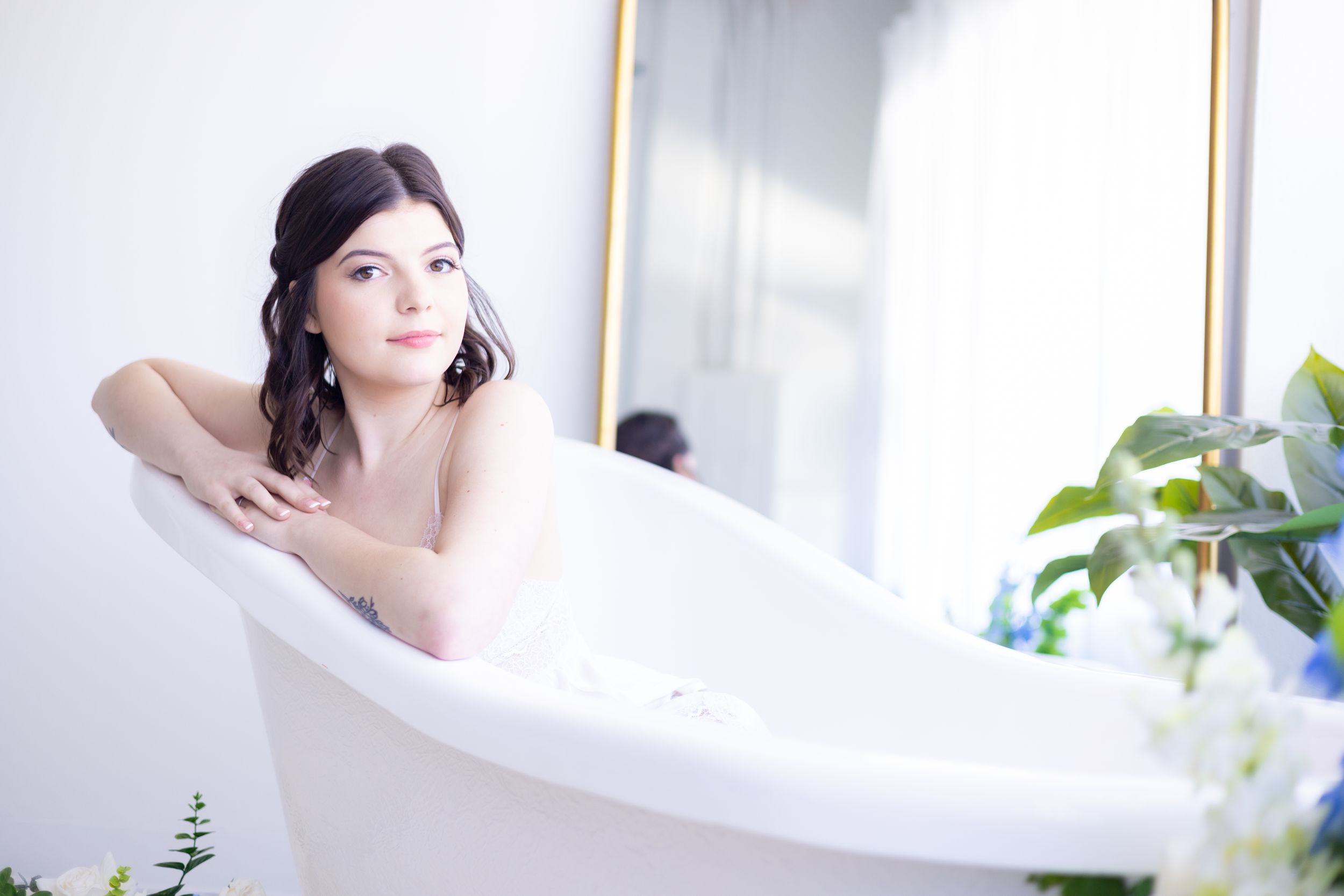Ethereal portrait in a white bathtub surrounded by natural light and indoor plants.