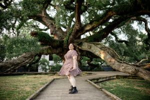 Person in a pink dress twirling on a wooden pathway under a massive spreading oak tree.