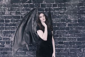 A dramatic portrait with dark wings against a brick wall background.