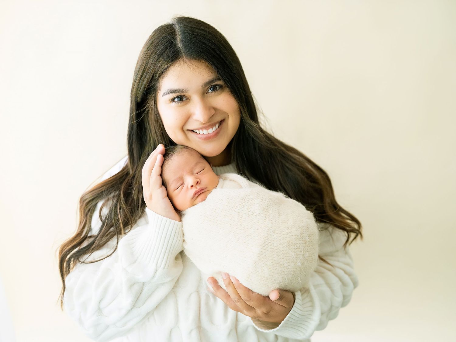 Close-up of newborn wrapped in cream blanket being cradled.