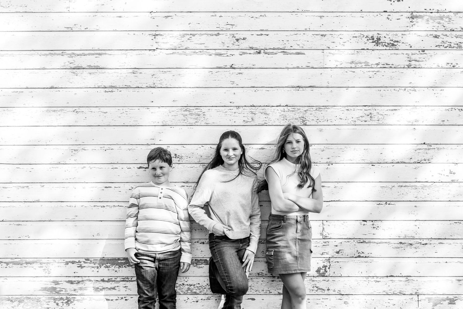 Group of children leaning against a rustic white wooden wall background.