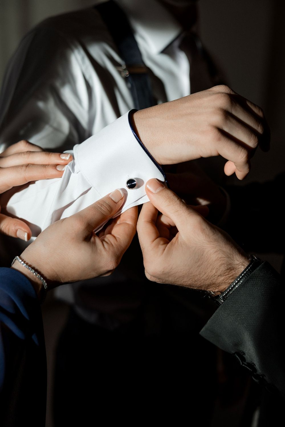 Close-up shot of hands adjusting white shirt cuffs with cufflinks in formal attire preparation.